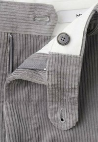 Tissu en velours côtelé gris avec nervures verticales, doté d'un bouton et d'une fermeture éclair, et d'une doublure blanche sur la ceinture pour un contraste supplémentaire.