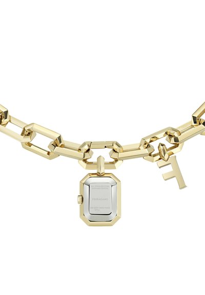 Kuldne massiivsete linkide kett, millel on poleeritud kellaketpendant ja väike tähe "F" charm, mis ripub linkide küljest, valgel taustal.