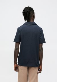 Tengerészkék rövid ujjú galléros póló, klasszikus gallérral, sima textúrával és laza szabással, világosbarna kordnadrággal párosítva.