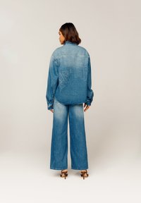 Denimjakke med stor "Take a Trip" broderi på baksiden, kombinert med vidde denimbukser, begge i en lys blå vask.