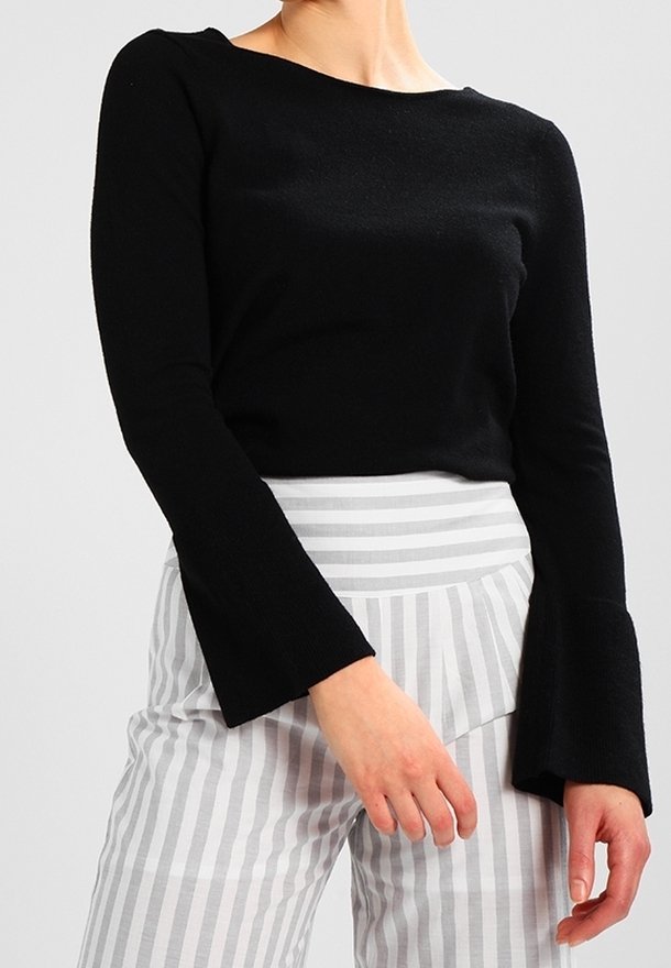 Musta pitkähihainen paita leveällä venepääntiellä ja kellohihansuilla, yhdistetty harmaa-valkoisiin raidoitettuihin korkeavyötäröisiin housuihin.