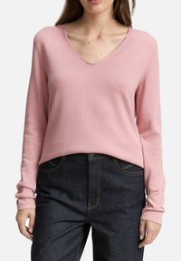 Pull-over rose clair en V en maille douce, avec des manches longues et une coupe décontractée. Associé à un jean en denim foncé.