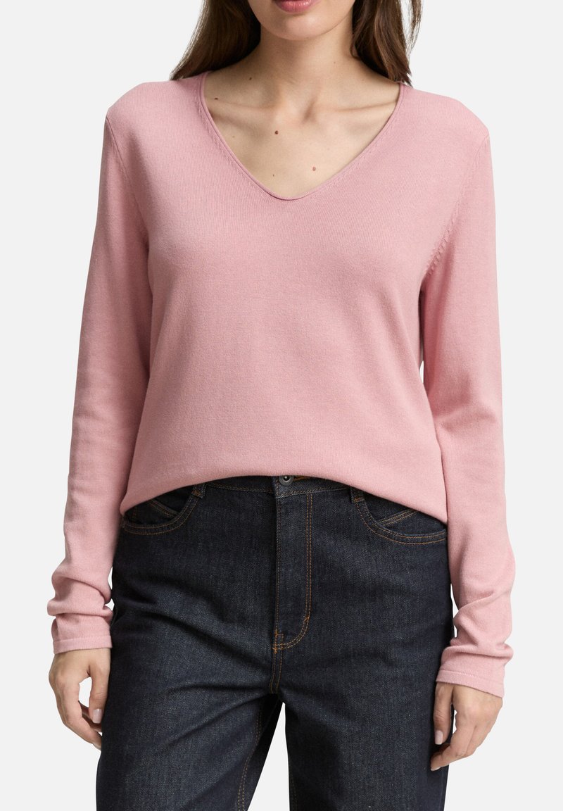 Pull-over rose clair en V en maille douce, avec des manches longues et une coupe décontractée. Associé à un jean en denim foncé.