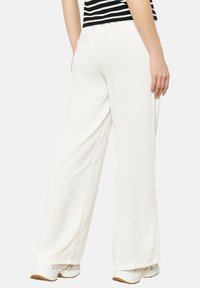 White wide-leg pants with a textured finish, featuring an elastic waistband and paired with white athletic shoes. Striped top partially visible.