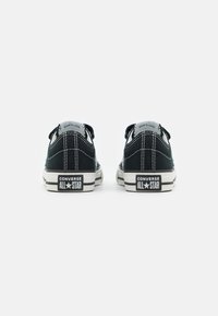 Svarte lerrets sneakers med hvite gummisåler, med svarte og hvite striper, kontrasterende sømmer, og "Converse All Star"-merket på hælen.