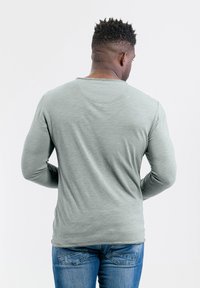Lange mouwen, lichtgroen shirt van zachte stof, met een ronde halslijn en achterkant naaddetail, gecombineerd met blauwe denim skinny jeans.