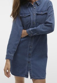 Denimskjortklänning i medelblått med långa ärmar, knäppning fram, två bröstfickor och avslappnad passform. Mjuk textur och klassisk design.