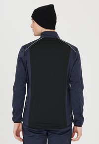 Schwarze und marineblaue Sportjacke mit hohem Kragen, langen Ärmeln und reflektierenden Akzenten auf den Schultern. Glatte Textur, taillierte Passform.