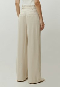Beige, weite Hosen aus karierter Stoff. Sie haben eine hohe Taille mit Gürtelschlaufen und zwei Gesäßtaschen; glatte Textur.