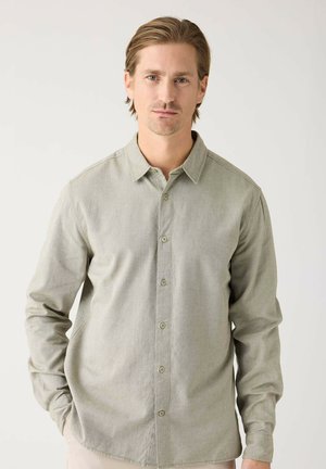 Camisa de manga larga verde claro hecha de tejido texturizado, con un cierre frontal de botones, cuello con solapa y bolsillos en las costuras laterales.