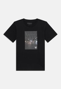 Schwarzes Baumwoll-T-Shirt mit einem rechteckigen Grafikdruck einer Stadtstraßenszene mit beleuchteten Gebäuden und einem dreieckigen Logo am unteren Rand.