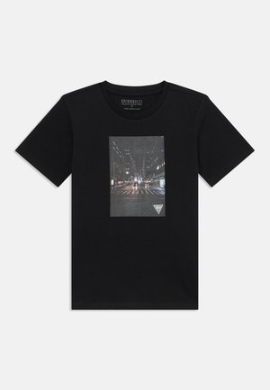 Black cotton t-shirt featuring a rectangular graphic print of a city street scene with lighted buildings and a triangular logo at the bottom.