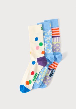 Tres calcetines coloridos con diferentes patrones: crema con puntos multicolores, azul claro con palomas blancas y estrellas, y a rayas con cruces.