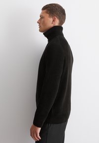 Black ribbed knit pullover with high collar, side zipper, and fitted design, shown from the side against a plain background.