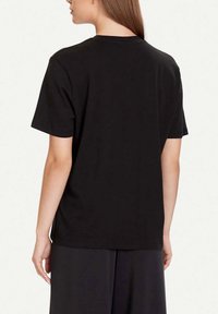 Camiseta negra de algodón con un corte holgado, mangas cortas y cuello redondo. Textura suave con un diseño sencillo, sin logotipos ni patrones visibles.