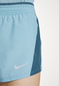 Shorts de sport bleu clair avec des panneaux latéraux bleu foncé et un logo Nike Swoosh blanc sur la partie avant de la jambe gauche.