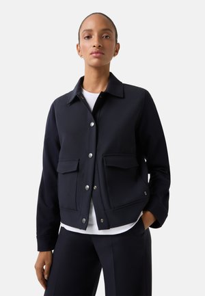Navy blue jacket made of smooth fabric, featuring a button-up front, two patch pockets, and a classic collar. Paired with a white shirt.