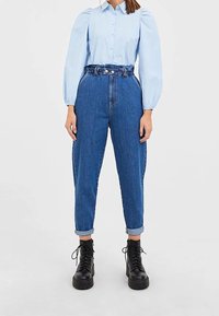 Light blue button-up shirt with puff sleeves, paired with high-waisted, rolled-up dark blue denim pants and black lace-up boots.