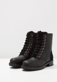 Czarne skórzane buty bojowe z teksturowanym mankietem z polaru, złotymi oczkami i gumową podeszwą z bieżnikiem zapewniającym przyczepność.