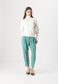 Maglione bianco fitted a collo alto in tessuto texturizzato; pantaloni teal su misura con pieghe; scarpe nere con tacco alto; borsa a spalla minimalista.