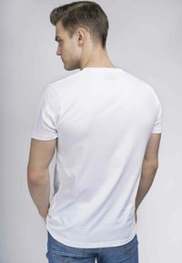 Hvid bomulds T-shirt med korte ærmer, rund halsudskæring og glat tekstur, båret med blå denim jeans, set bagfra.