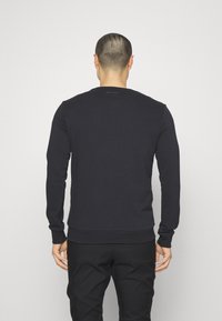 Felpa nera a maniche lunghe con polsini e orlo a costine. Caratterizzata da un collo rotondo e un piccolo logo sul retro. Realizzata in tessuto morbido.