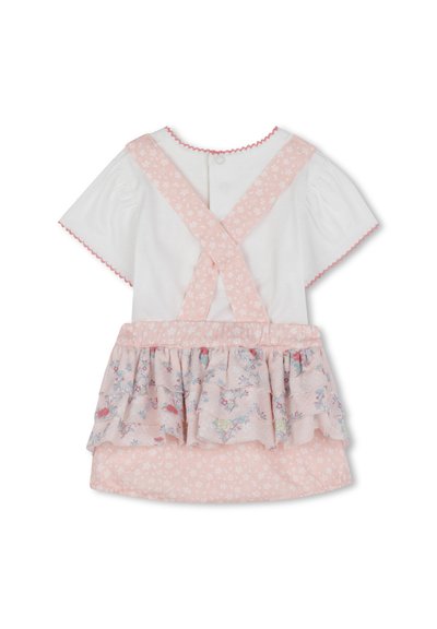 Haut blanc à manches courtes, jupe rose à volants avec motifs floraux, et bretelles croisées. Bords découpés. Fermeture à boutons au dos.