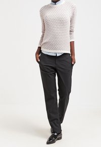 Maglione lavorato a maglia grigio chiaro con motivo e collo tondo indossato su una camicia col blu chiaro, abbinato a pantaloni scuri su misura e scarpe nere.