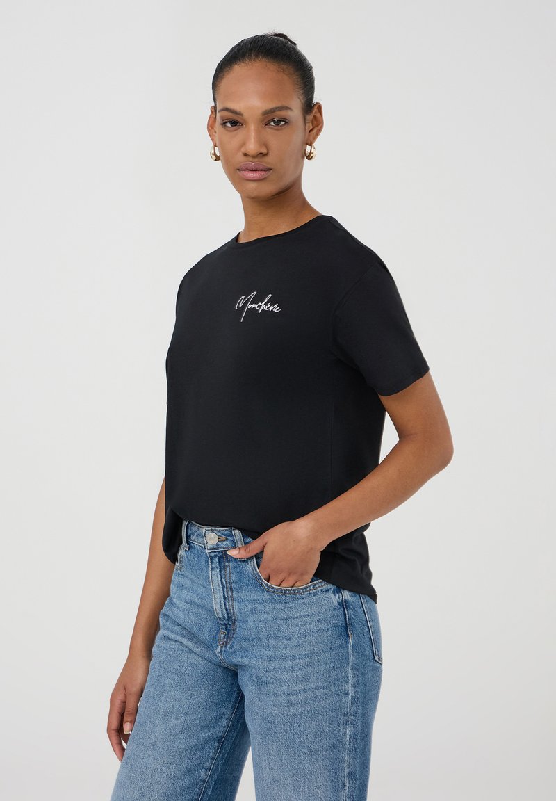 T-shirt nera con scollo rotondo e maniche corte, con un logo discreto sul petto, abbinata a jeans di denim blu a vita alta.