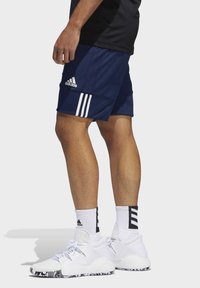 Marineblaue Sportshorts mit drei weißen Streifen, kombiniert mit weißen Sneakers mit strukturiertem Obermaterial und gemusterter Gummisohle. Weiße Socken inklusive.