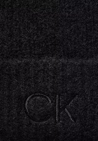 Berretto lavorato a maglia nero realizzato in morbida lana con una finitura testurizzata. Presenta il logo "CK" ricamato in filo nero abbinato.