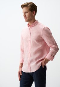 Baumwollmischhemd in hellrosa mit feinem Streifenmuster, Button-Down-Kragen und langen Ärmeln, kombiniert mit dunkel gefärbten Hosen.
