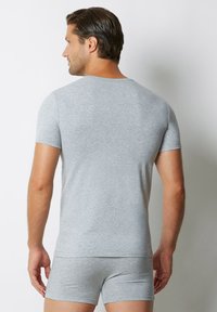 Szary bawełniany t-shirt z krótkim rękawem i prążkowanym dekoltem, noszony z dopasowanymi szarymi bokserkami. Charakteryzuje się dopasowanym krojem i gładką teksturą.