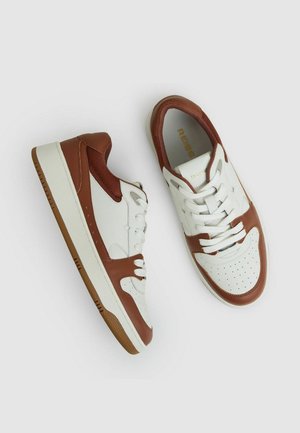Sneakers con tomaia in pelle bianca e dettagli marroni. Presentano una punta forata, un design con lacci e una suola in gomma con finitura testurizzata.