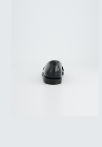 Zwarte leren instappers met een gladde textuur, lage hak en gestikte details. Rond neus en subtiel logo op de zijkant geperst.