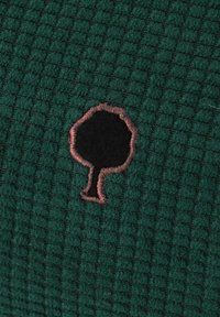 Groene textuurstof met een geborduurde zwarte boomsilhouet omrand met een roze draad in het midden.