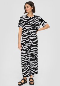 Ensemble en imprimé zèbre noir et blanc, composé d'un haut à manches courtes et d'un pantalon large, fabriqué dans un tissu léger et texturé. Des sandales noires complètent le look.