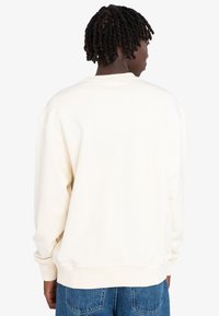 Cream-colored sweatshirt with a relaxed fit, ribbed cuffs, and a round neckline, featuring a smooth texture. Back view showing no graphics.