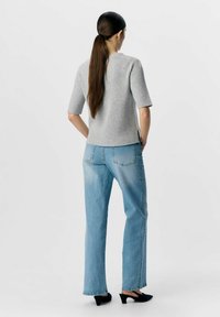 Maglione grigio a righe con maniche corte, jeans a vita alta blu chiaro e mule nere con tacco. I jeans presentano un lavaggio leggermente sbiadito.