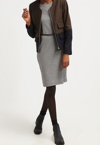 Veste courte marron et marine avec fermeture éclair, robe à motifs noir et blanc, collants noirs et bottines. Design ajusté avec poches.