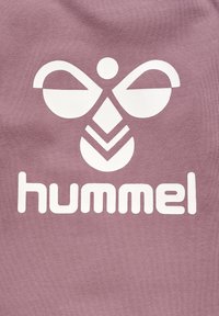 Lilla stof med et stort, hvidt logo bestående af abstrakte former og ordet "hummel" i store, fede bogstaver.