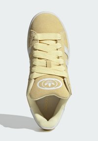 Zapatillas de ante amarillo con acentos blancos, que cuentan con cordones planos, un collar acolchado y un logo circular en la lengüeta.