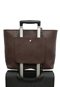 Pruun nahast käekott tekstuuriga pinnaga, millel on eesmine tasku ja hõbedased riistad, asetatud musta kohvri kohale, millel on laiendatav käepide.