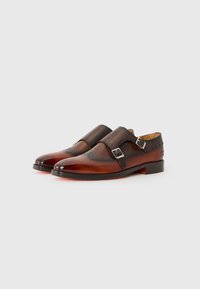 Zapatos de cuero marrón de doble hebilla con un acabado suave, perforaciones decorativas a lo largo de las costuras y un diseño de punta ligeramente puntiaguda.