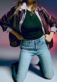 Burgundy läder bomberjacka över en svart tajt topp, tillsammans med ljusblå högmidjade jeans. Randig krage synlig.