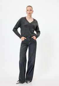 Pull en tricot gris avec un col en V, associé à un jean large gris foncé. La tenue présente une coupe décontractée et des chaussures argentées à bout pointu.