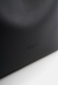 Bolso de cuero negro con textura lisa, branding sutil y diseño minimalista. Sin herrajes ni detalles visibles.