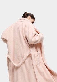 Rosa, fluffig, överdimensionerad morgonrock med en mjuk textur, som har en krage, sidofickor och en bälteaccent. Tyget verkar mysigt och varmt.