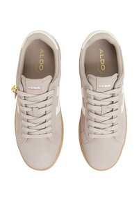 Sneaker beige con texture liscia, con strisce bianche, lacci piatti e suola in gomma. Branding visibile sulla linguetta.
