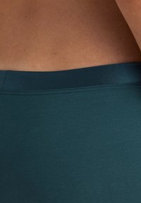 Diepblauwe, aansluitende stof tailleband van leggings met een gladde textuur. Het materiaal lijkt rekbaar en lichtgewicht, met een nette afwerking.